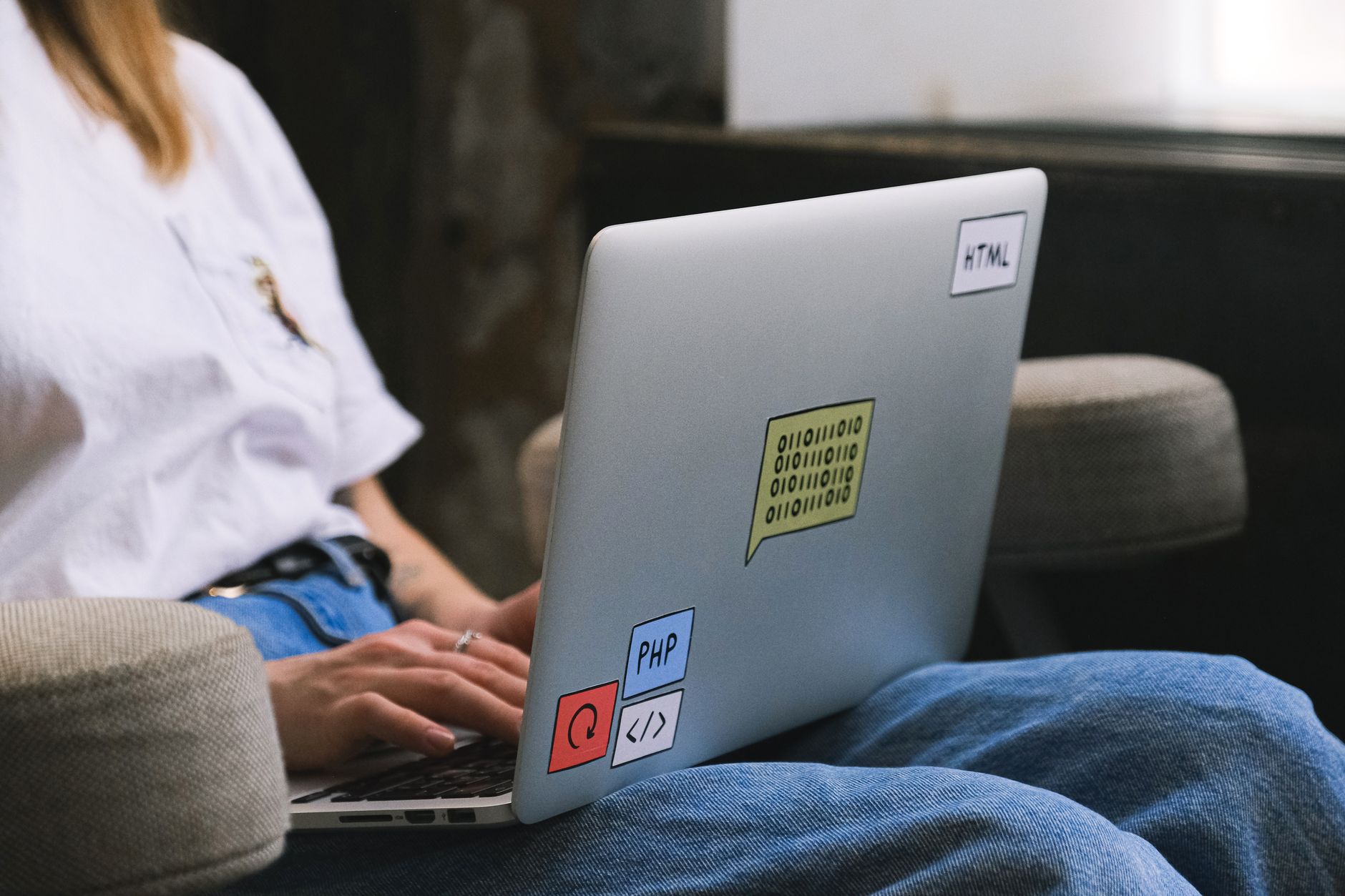 Personne tapant sur un ordinateur portable avec autocollants de codage, symbolisant le travail à distance et le travail indépendant.