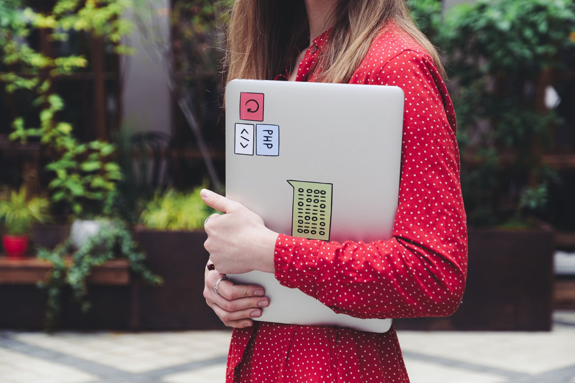 Une jeune femme en chemisier à pois rouges tient un ordinateur portable avec autocollants à l'extérieur.