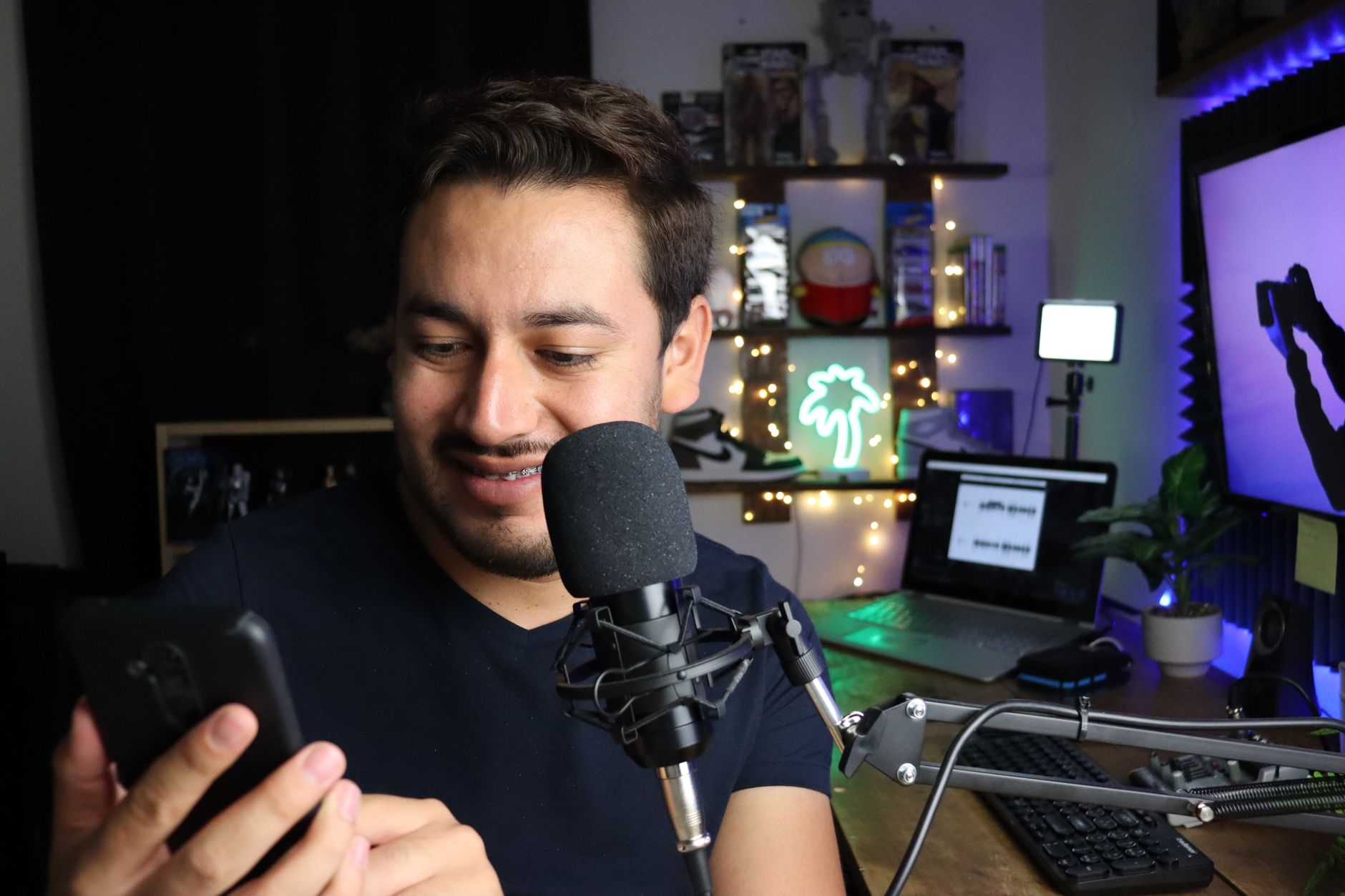 Un homme utilise un smartphone assis à un bureau avec un microphone, entouré d'une décoration confortable.