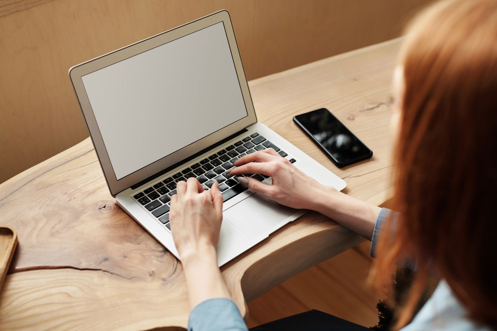 Une femme travaille sur un ordinateur portable à un bureau en bois, à l'intérieur avec lumière naturelle.